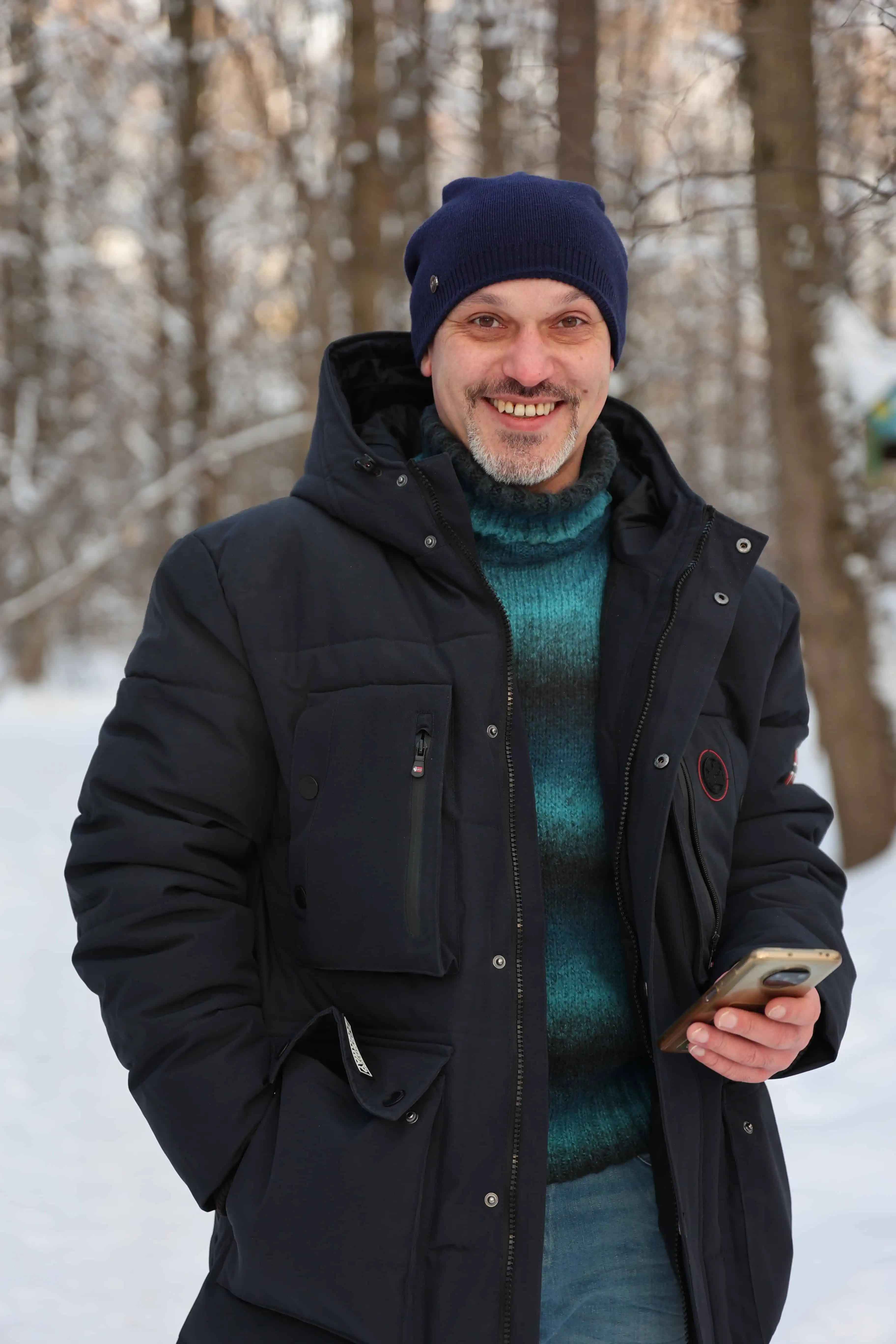 A picture of a smiling man in winter clothing standing in the snow.